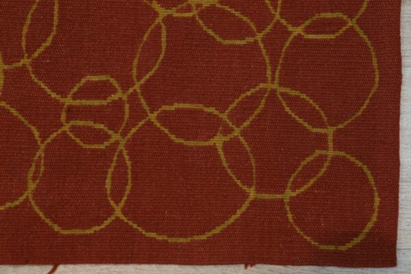 Detail view of a low-pile rust rug featuring interlocking yellow-green circles on light wood flooring.