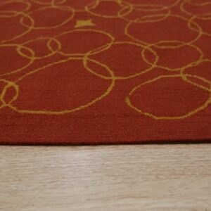 A terracotta low-pile rug with looping yellow circles and a star rests on light wood flooring.