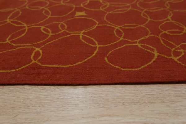 A terracotta low-pile rug with looping yellow circles and a star rests on light wood flooring.