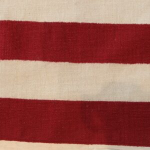 Close-up of a flatwoven rug with broad red and cream horizontal stripes resting on wood.