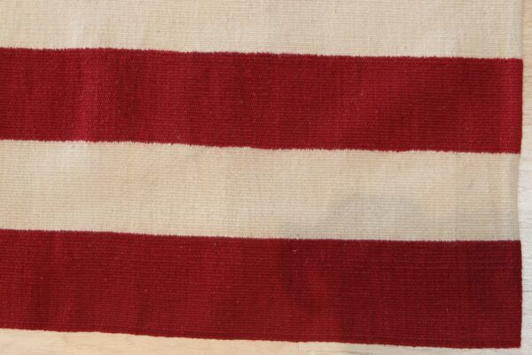 Close-up of a flatwoven rug with broad red and cream horizontal stripes resting on wood.
