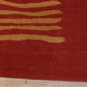 Detail of a flatweave rug with abstract golden stripes against a red background on light wood planks.