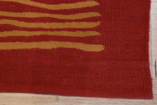 Detail of a flatweave rug with abstract golden stripes against a red background on light wood planks.