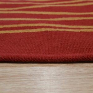 Red flatweave rug with wavy gold stripes rests closely on light wooden plank flooring.