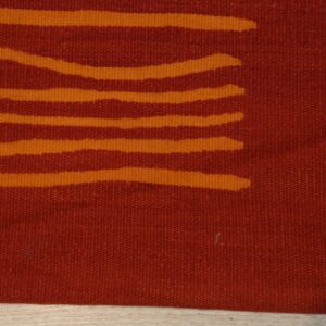 A rust-colored flatweave rug with abstract orange horizontal stripes rests on light wood flooring.