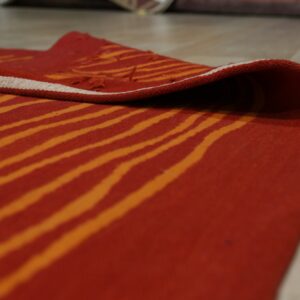 A rust and orange wavy striped rug is partially rolled up on light wood flooring.