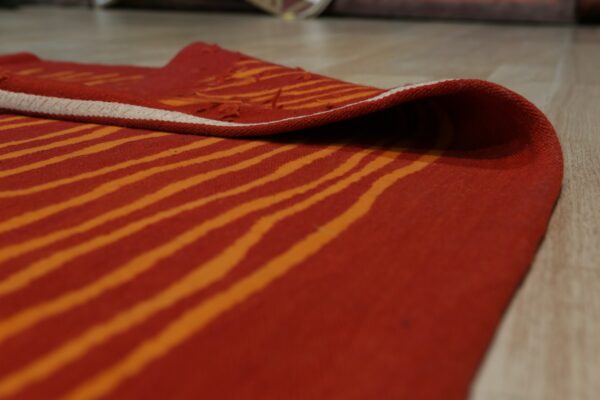 A rust and orange wavy striped rug is partially rolled up on light wood flooring.