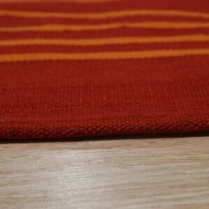 Close-up of a low-pile rug featuring red and bright orange horizontal stripes resting on light wood flooring.