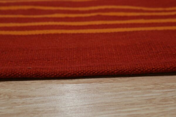 Close-up of a low-pile rug featuring red and bright orange horizontal stripes resting on light wood flooring.