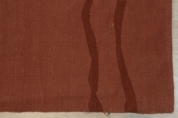 Close-up of a terracotta flatweave rug with two darker wavy stripes on light wood floor.