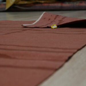Terracotta low-pile rug with subtle stripes, partially folded back, showing a yellow tag on light wood flooring.