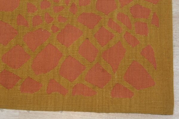 Flatweave rug with a terracotta and mustard yellow irregular geometric pattern on light wood floor.