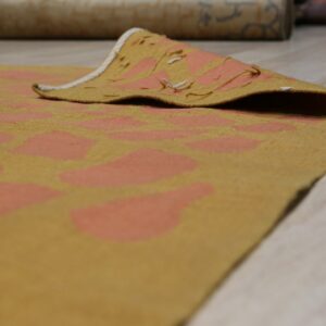 Low-pile gold and coral abstract patterned rug with a curled edge on light wood flooring.