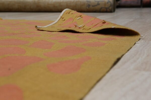 Low-pile gold and coral abstract patterned rug with a curled edge on light wood flooring.