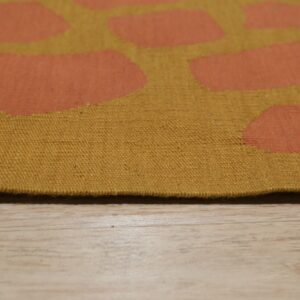 Mustard flatweave rug with orange abstract shapes rests on light wood plank flooring.