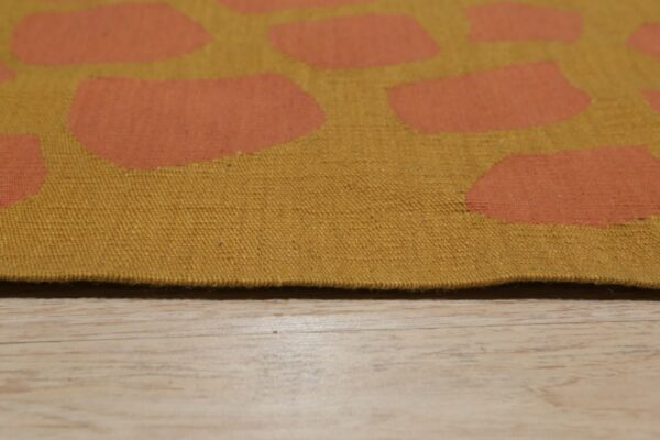 Mustard flatweave rug with orange abstract shapes rests on light wood plank flooring.