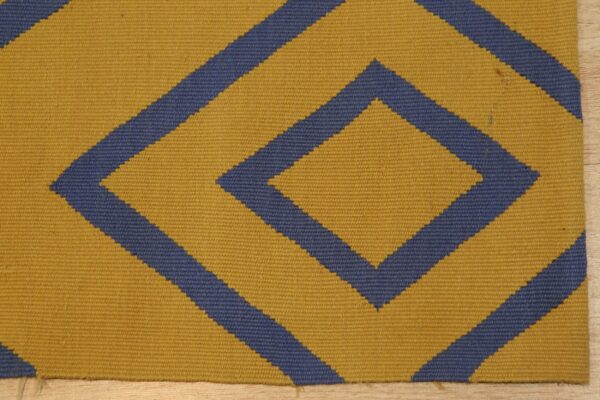 Low pile rug with yellow and blue geometric diamond pattern resting on light wood flooring.