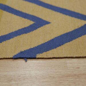 Close-up of a yellow and blue geometric flatweave rug edge resting on light colored wood planks.