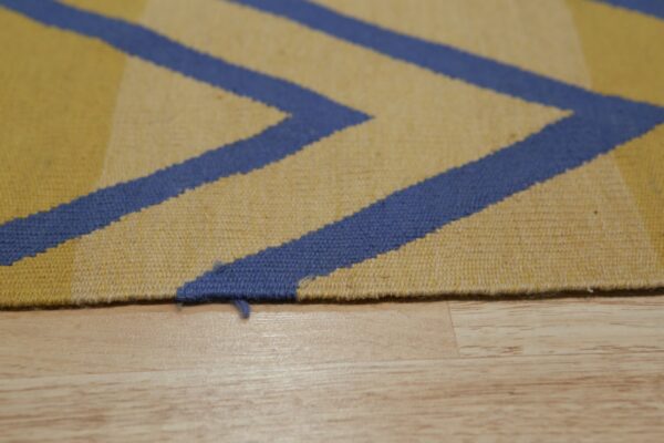 Close-up of a yellow and blue geometric flatweave rug edge resting on light colored wood planks.