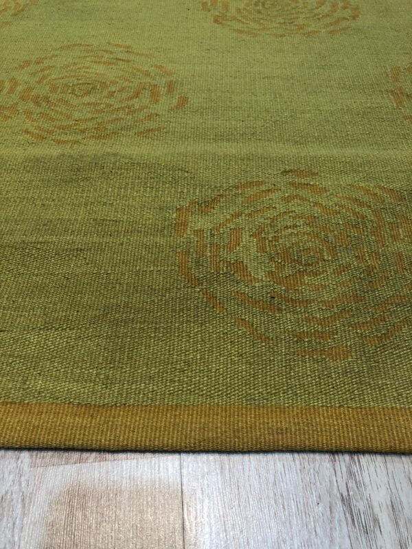 Olive green flatweave rug featuring abstract rusty orange circular designs resting on light wood flooring.