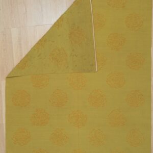 Chartreuse flatweave rug with orange swirl patterns, folded to show the reverse side on light wood flooring.