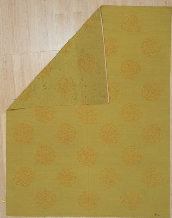 Chartreuse flatweave rug with orange swirl patterns, folded to show the reverse side on light wood flooring.
