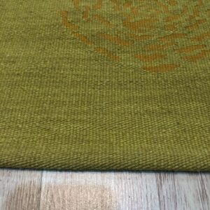 Tightly woven olive green rug featuring a partial gold abstract pattern, displayed on light wood-look flooring.
