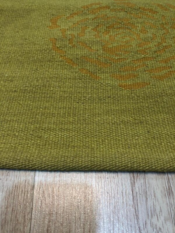 Tightly woven olive green rug featuring a partial gold abstract pattern, displayed on light wood-look flooring.