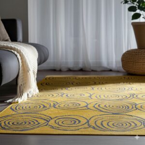 A yellow and blue concentric circle rug lies on dark flooring next to a dark sofa and rattan pouf.