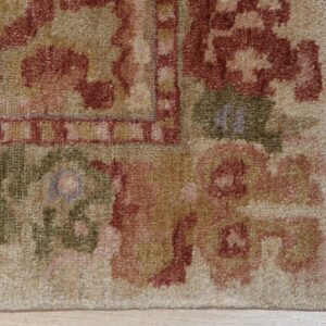 Beige, terracotta, and green patterned rug edge with visible fringe rests on light wood flooring.