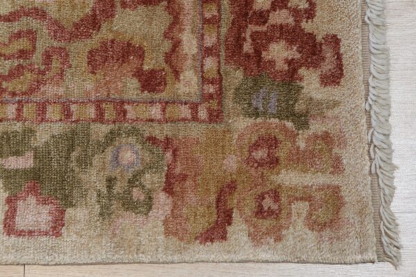 Beige, terracotta, and green patterned rug edge with visible fringe rests on light wood flooring.