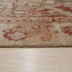Low-angle detail shot of a beige rug edge with rust patterns on light wood flooring.