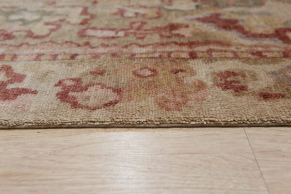 Low-angle detail shot of a beige rug edge with rust patterns on light wood flooring.