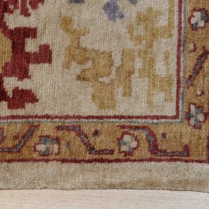 A high-texture rug featuring cream, red, and gold geometric patterns and a detailed border on wood flooring.
