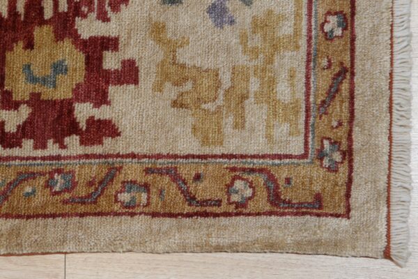 A high-texture rug featuring cream, red, and gold geometric patterns and a detailed border on wood flooring.