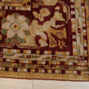 Traditional high-pile rug corner featuring red, gold, and green floral and geometric patterns on light wood flooring.