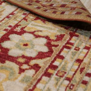 A traditional cream, red, and gold pile rug is folded back revealing its flat woven backing on light flooring.