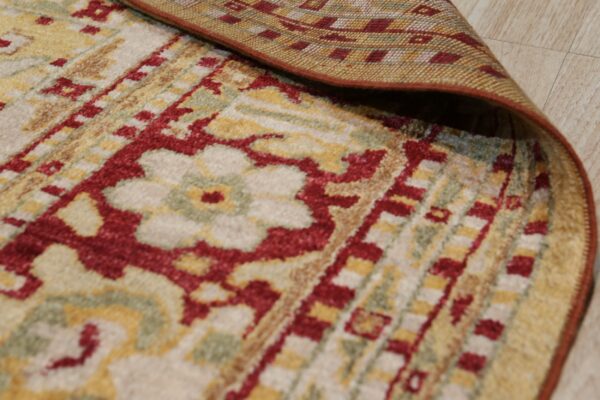 A traditional cream, red, and gold pile rug is folded back revealing its flat woven backing on light flooring.