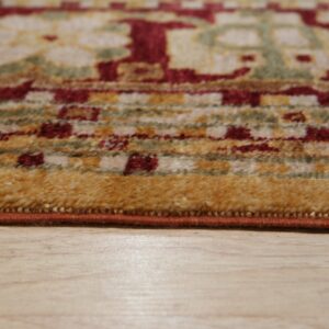 The edge of a medium-pile rug features red, gold, and green traditional patterns over light wood flooring.