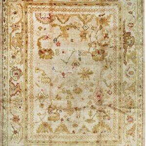 Light beige rug with traditional faded gold, rust, and green floral and geometric patterns and fringe.