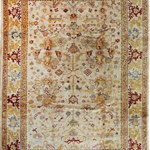 Rectangular area rug with an ivory field and distressed traditional motifs in gold, rust red, and slate blue.