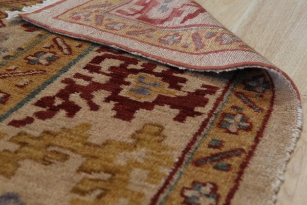 A patterned beige, gold, and terracotta rug with short pile is curled back on light wood flooring.
