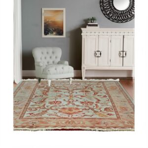 Light blue and orange traditional rug under a tufted gray armchair and white cabinet.