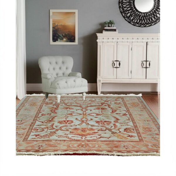 Light blue and orange traditional rug under a tufted gray armchair and white cabinet.