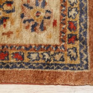 High-pile traditional rug corner in beige, blue, and terracotta on light wood, showing tassels.