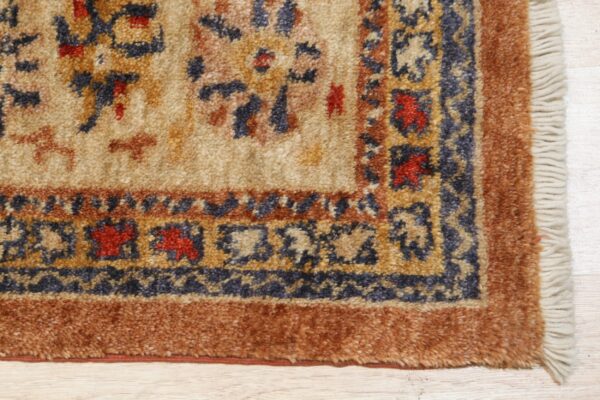 High-pile traditional rug corner in beige, blue, and terracotta on light wood, showing tassels.