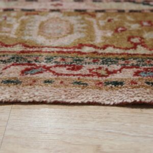 Multicolored high-pile rug edge featuring red, tan, and green rests on light wood plank flooring.