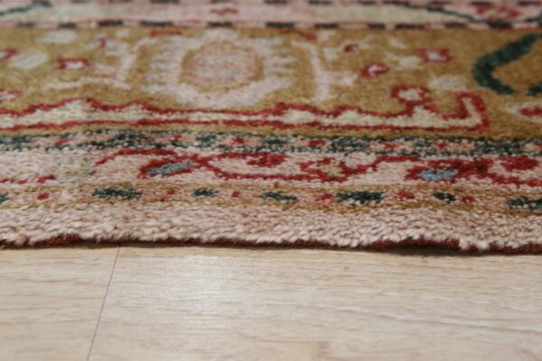 Multicolored high-pile rug edge featuring red, tan, and green rests on light wood plank flooring.