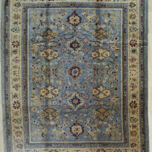 A traditional blue rug with gold, red, and navy floral patterns rests upon light wood flooring.