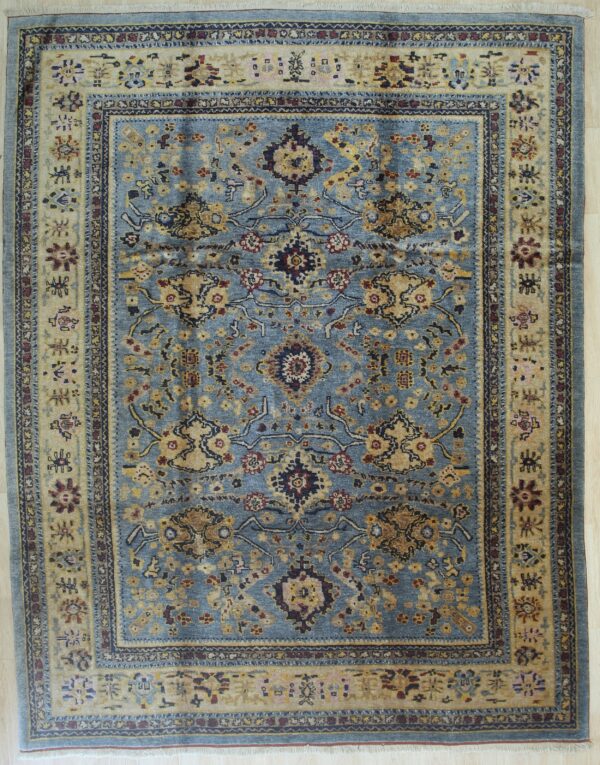 A traditional blue rug with gold, red, and navy floral patterns rests upon light wood flooring.